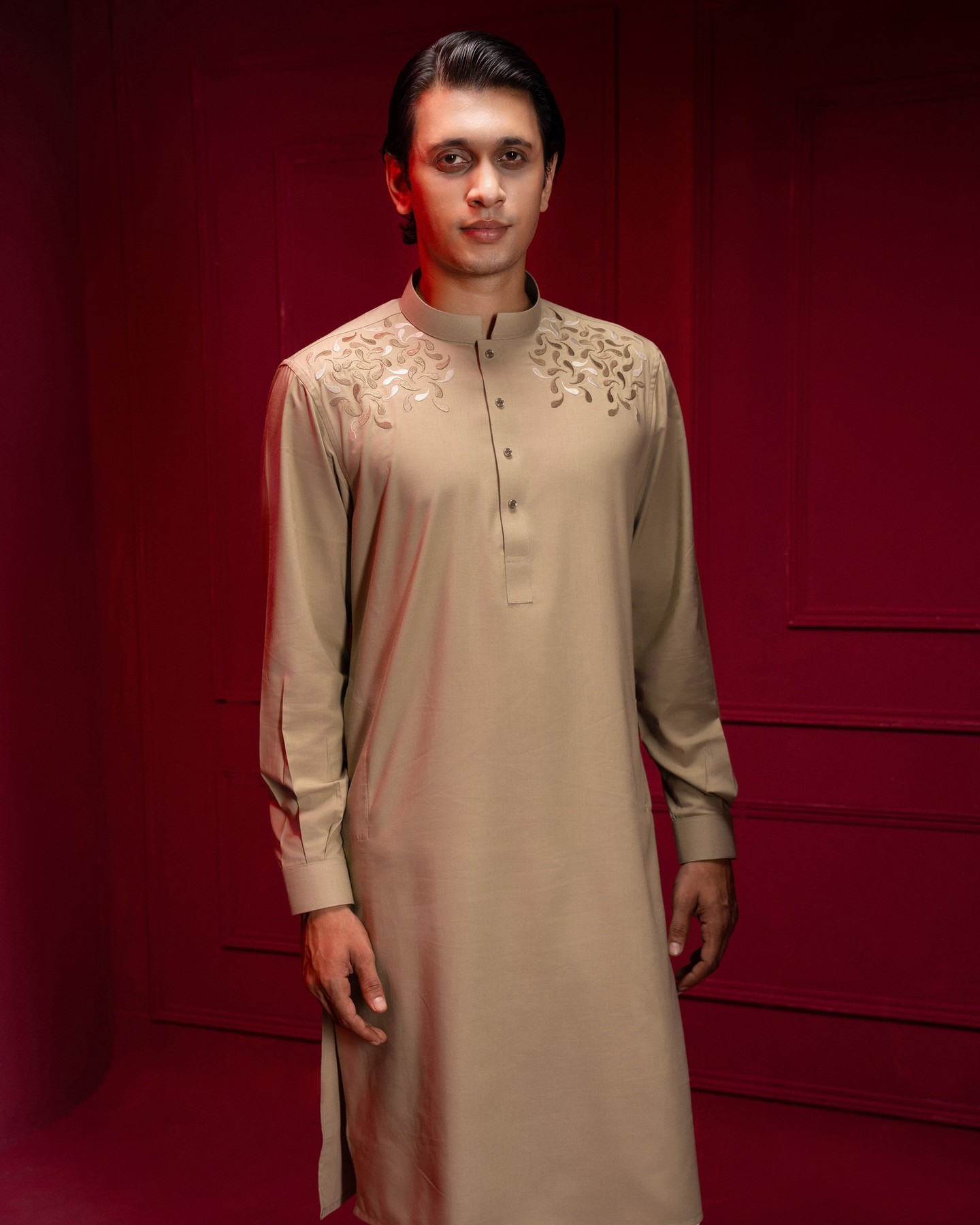 Model in a beige VIOR panjabi with tonal embroidery across the shoulders, against the deep red wall