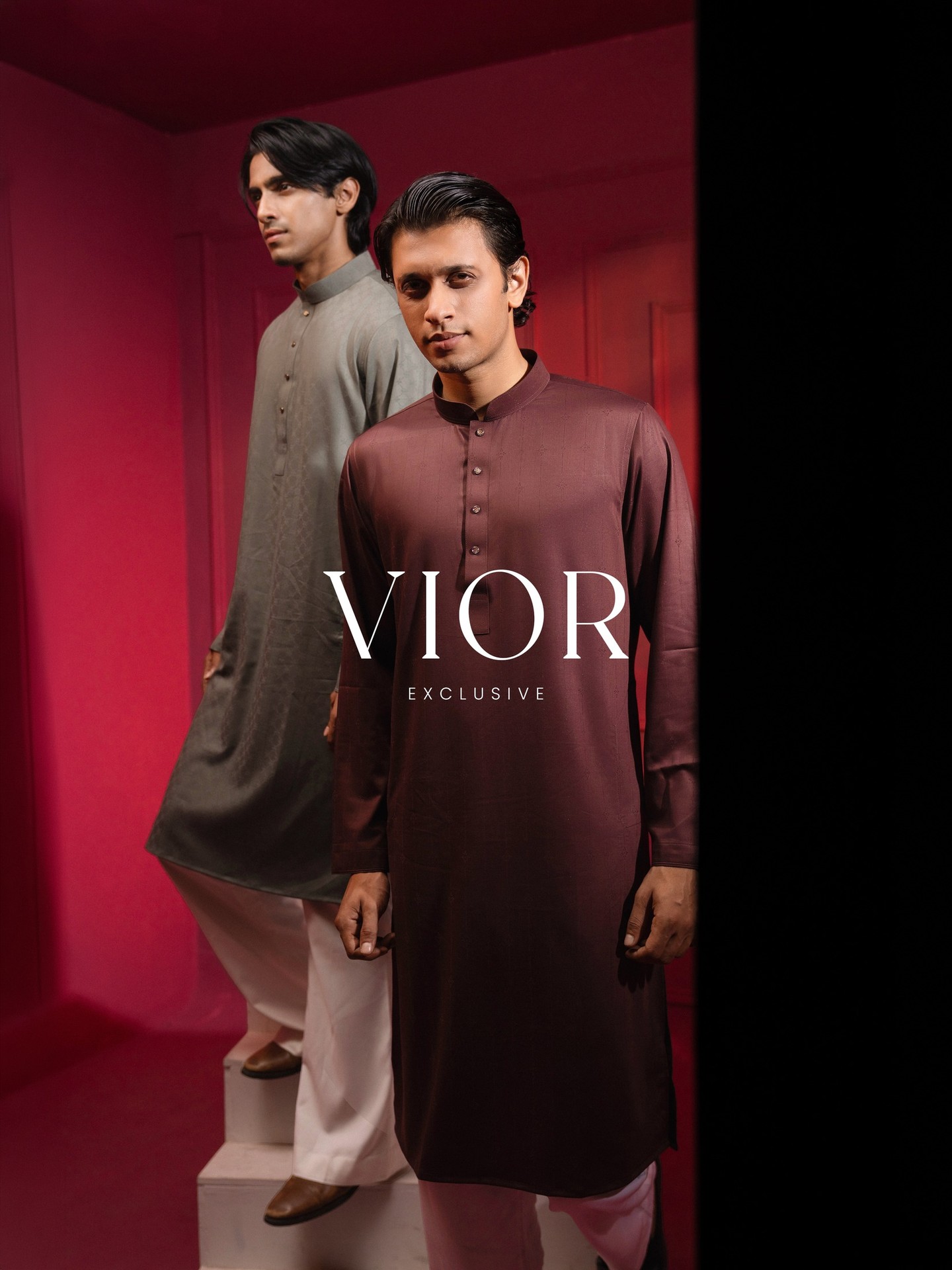 Two models in VIOR panjabis on the white steps of the red room, beneath the VIOR Exclusive wordmark