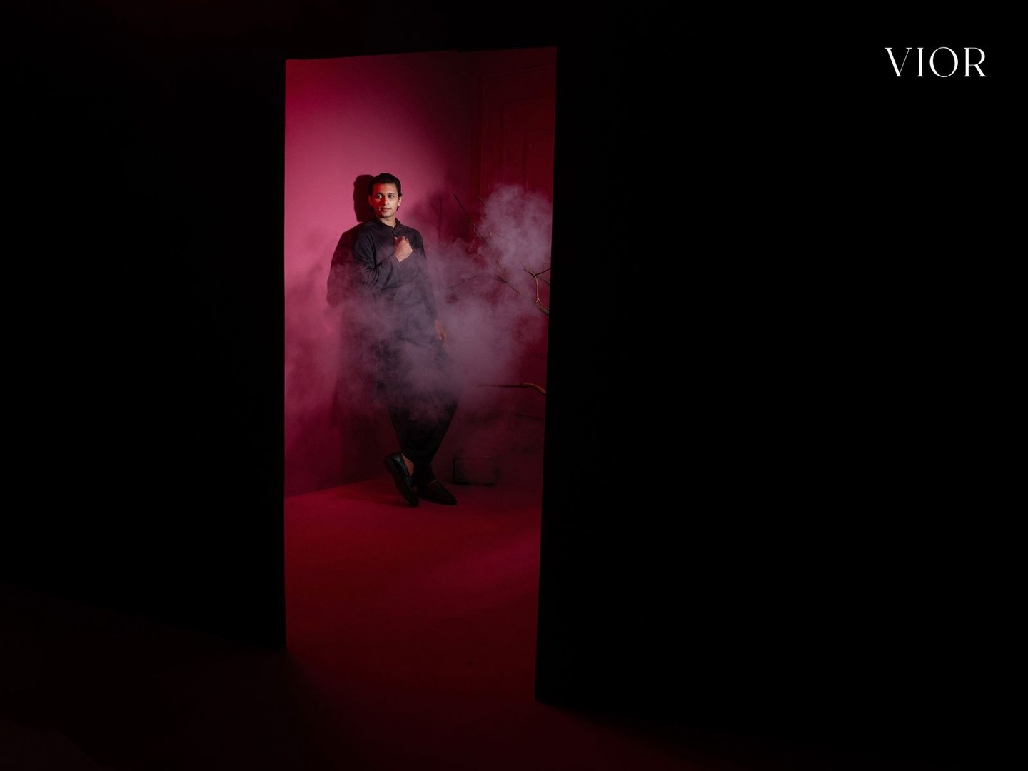 A man in black stands in a smoke-filled doorway of the red room, beside the VIOR wordmark